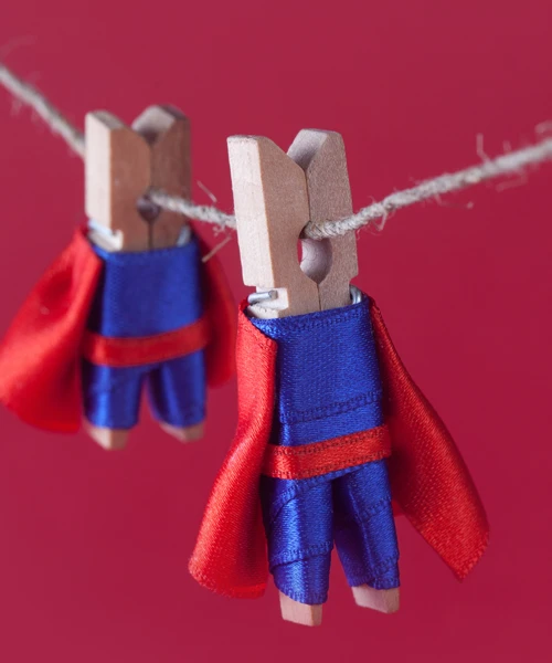 Two clothespins on a line dressed as superheroes