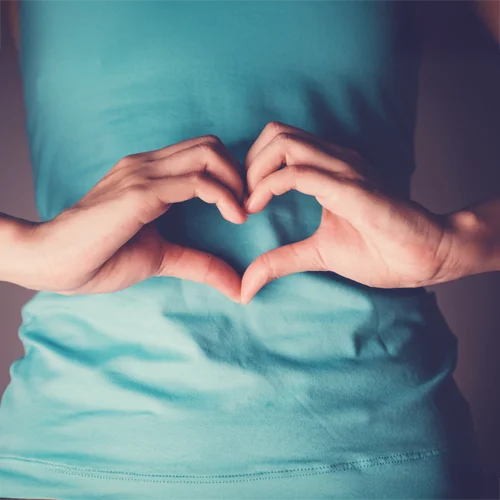 Hands held in a heart shape over the top of a woman's stomach